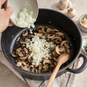 K opečeným šampiňónom sa v hrnci pridáva nakrájaná cibuľa a cesnak.